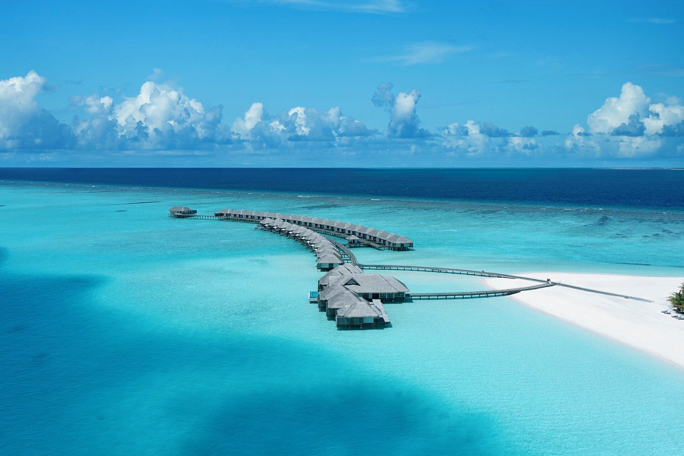 Eine Luftaufnahme von überwasserbungalows, die durch eine Brücke über türkisfarbenes Wasser verbunden sind.