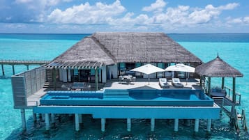 Een overwater villa met een zwembad, rieten dakken en uitzicht op de oceaan.