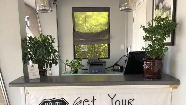 A reception desk with a Route 66 sign, a map, and two potted plants. - Mountain View Inn (Flagstaff)