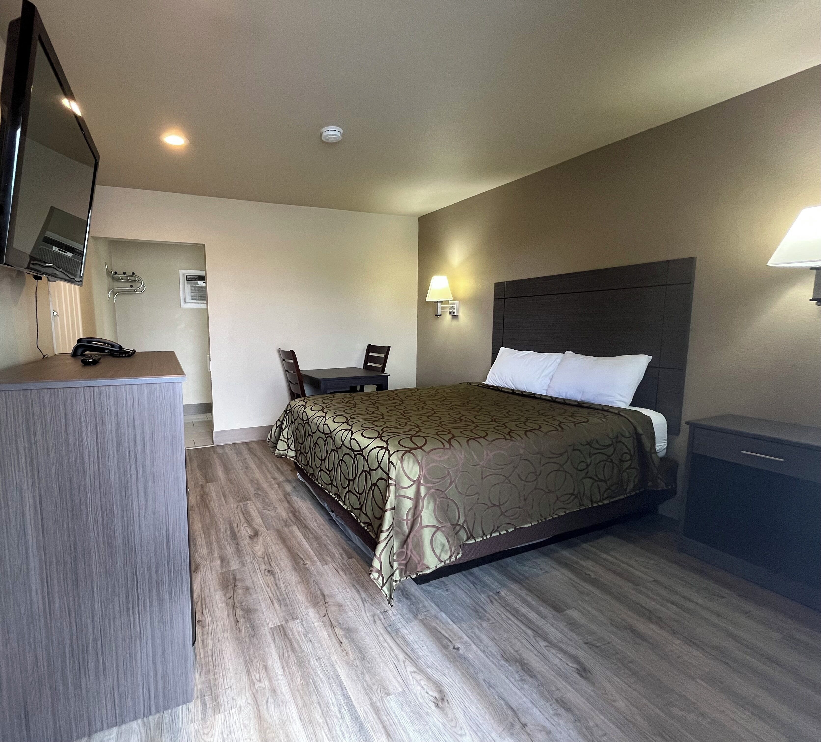 A hotel room with a bed, bedside table, lamp, desk, chair, and a telephone.