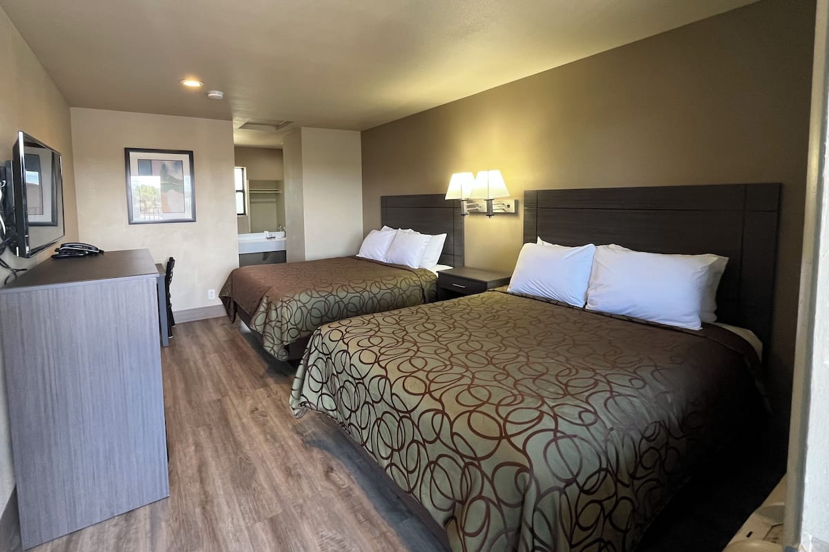 A hotel room with two beds, a desk, a TV, and a bathroom.