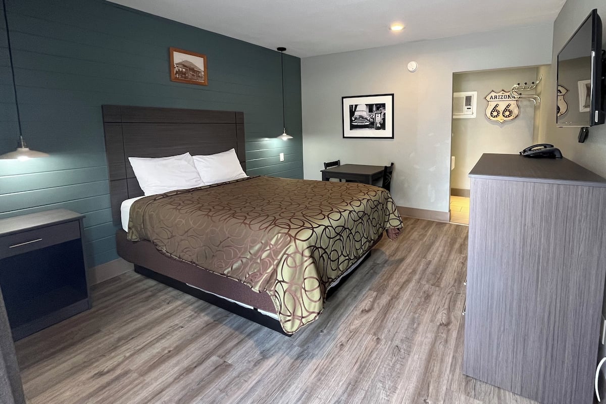 A hotel room with a bed, bedside tables, a desk, a mirror, and a wall clock.