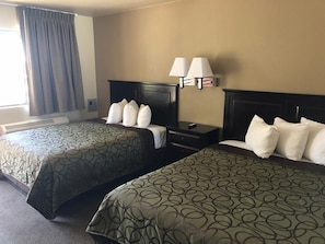 A hotel room with two beds, a nightstand, a lamp, and a window with curtains.