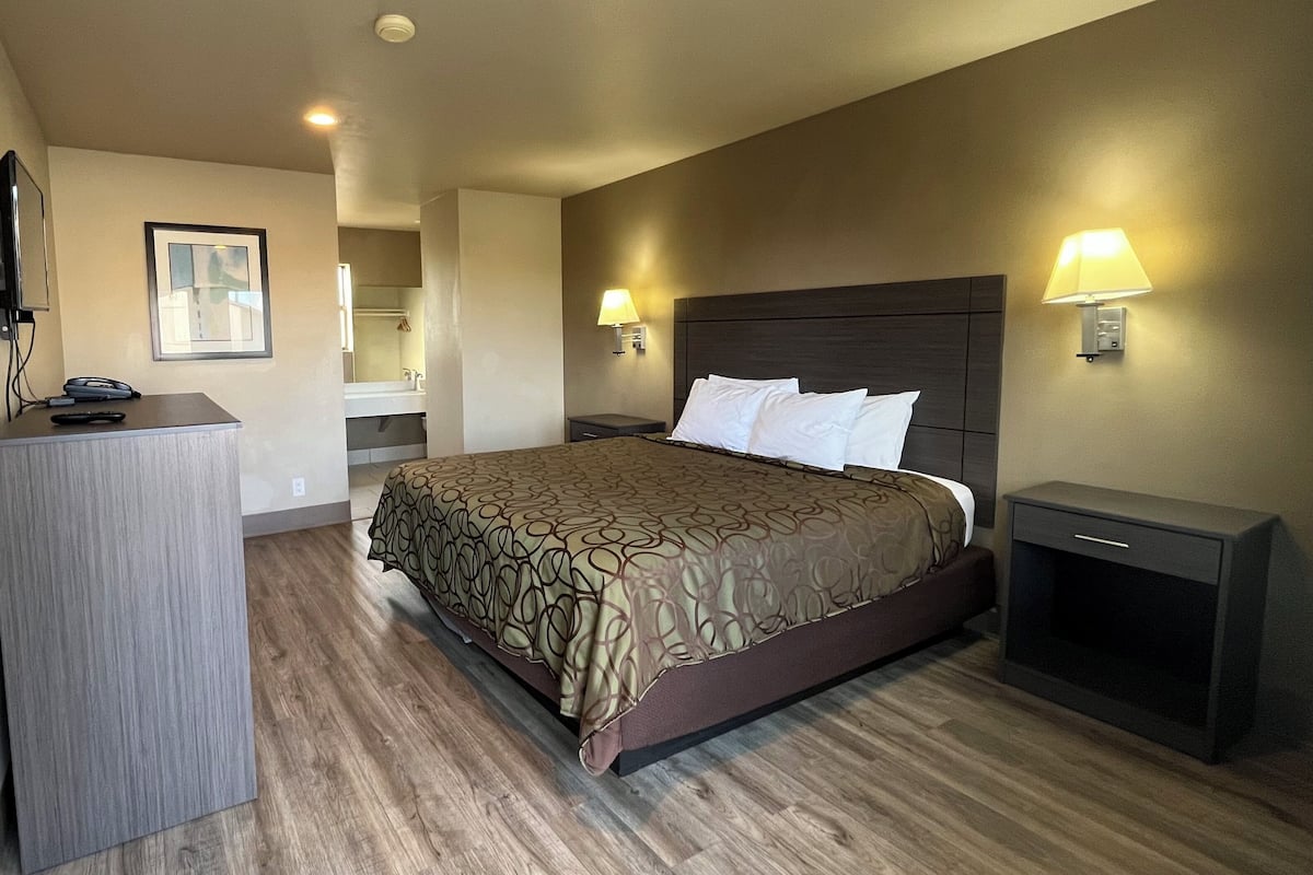 A hotel room with a large bed, bedside lamps, a desk with a chair, a mirror, and a television.