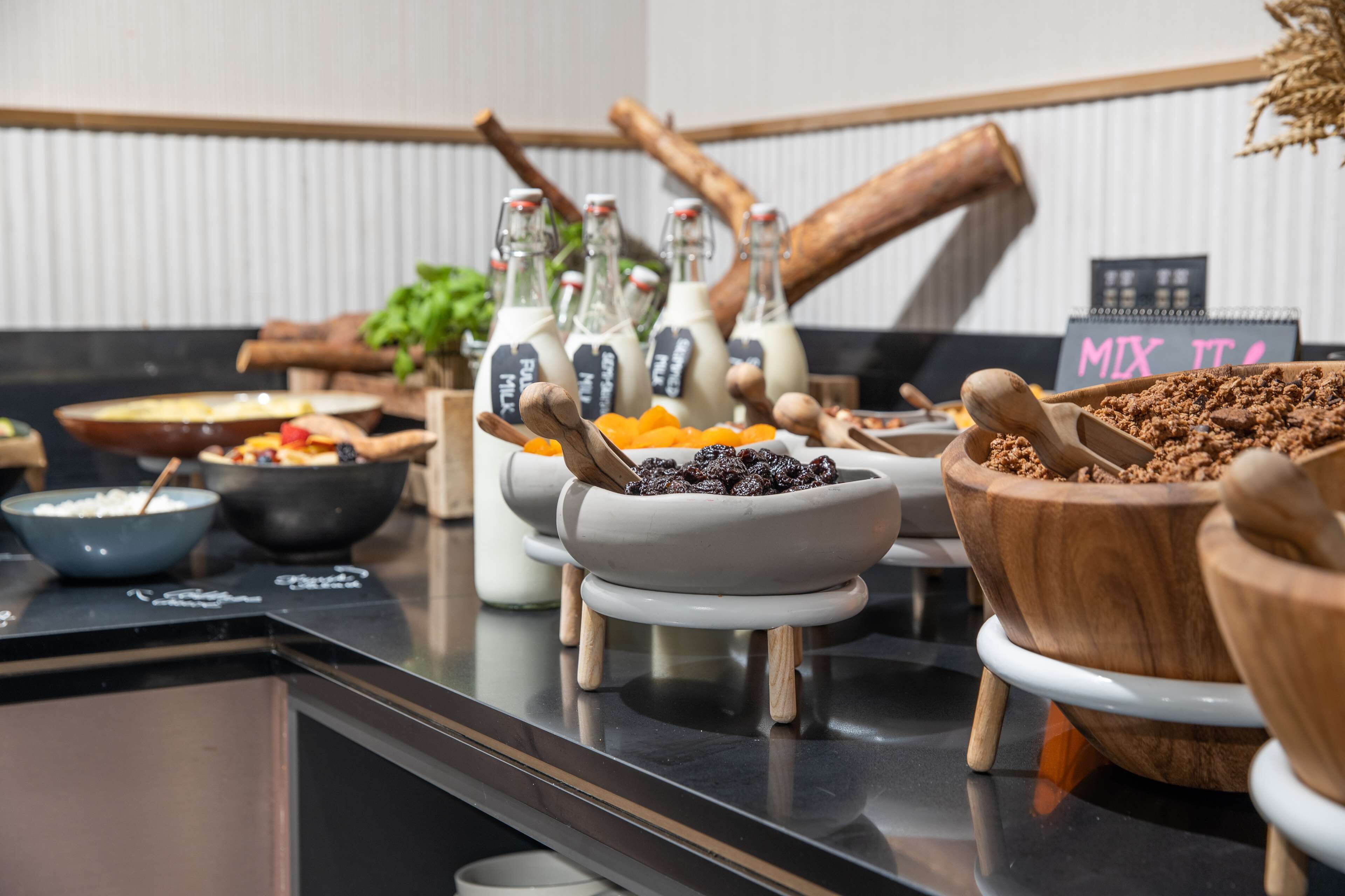 Een buffet met diverse gerechten en drankjes, waaronder schalen met fruit, noten en een bord met de tekst 