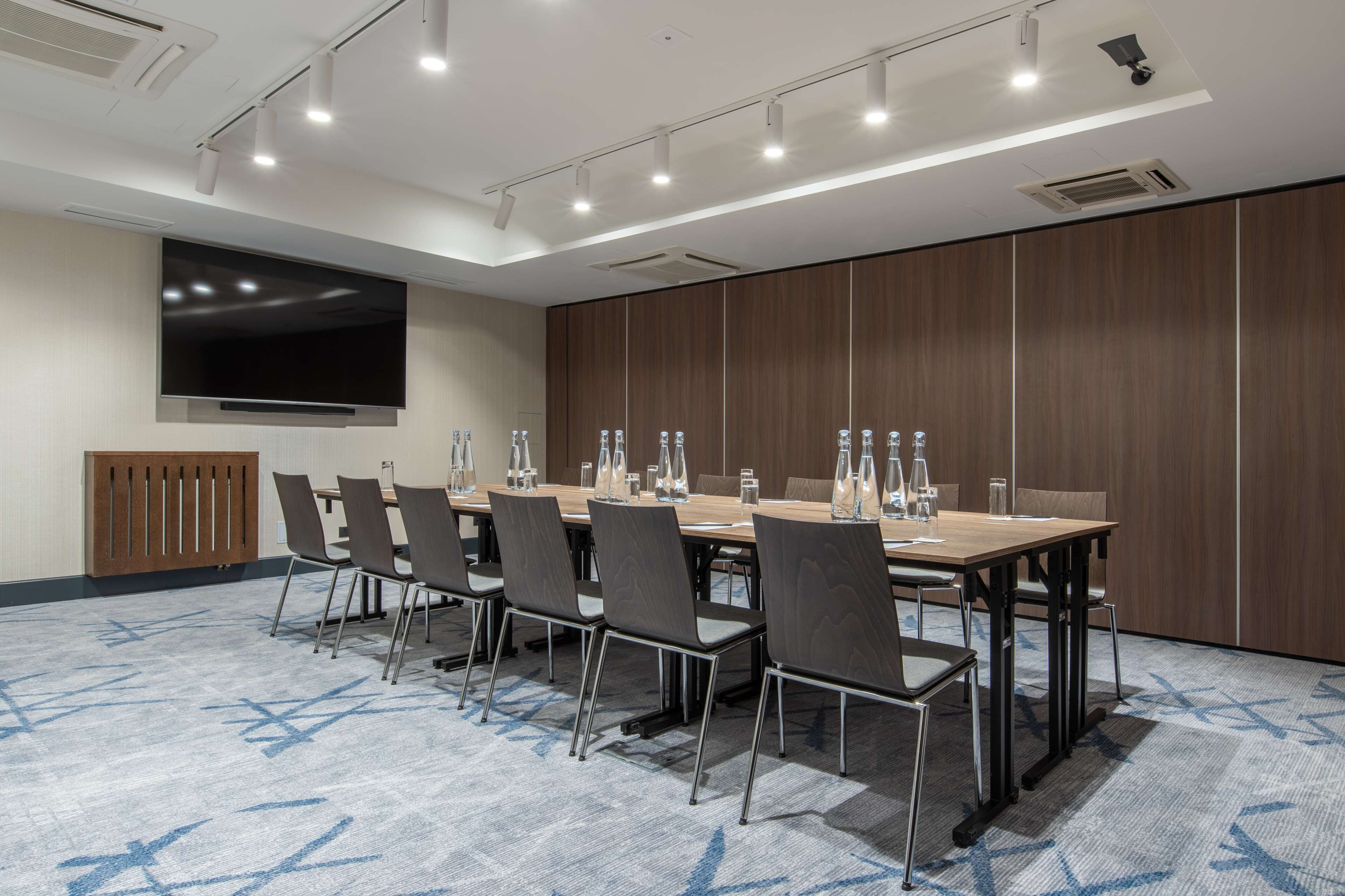 A conference room with a long table, chairs, a flat-screen TV, and a large window.