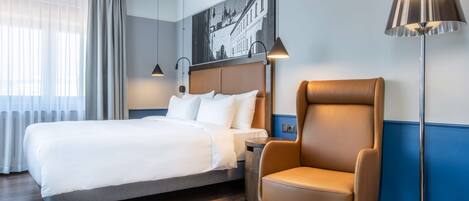 Una habitación de hotel con una cama, una silla, una lámpara de pie y un cuadro colgado en la pared.