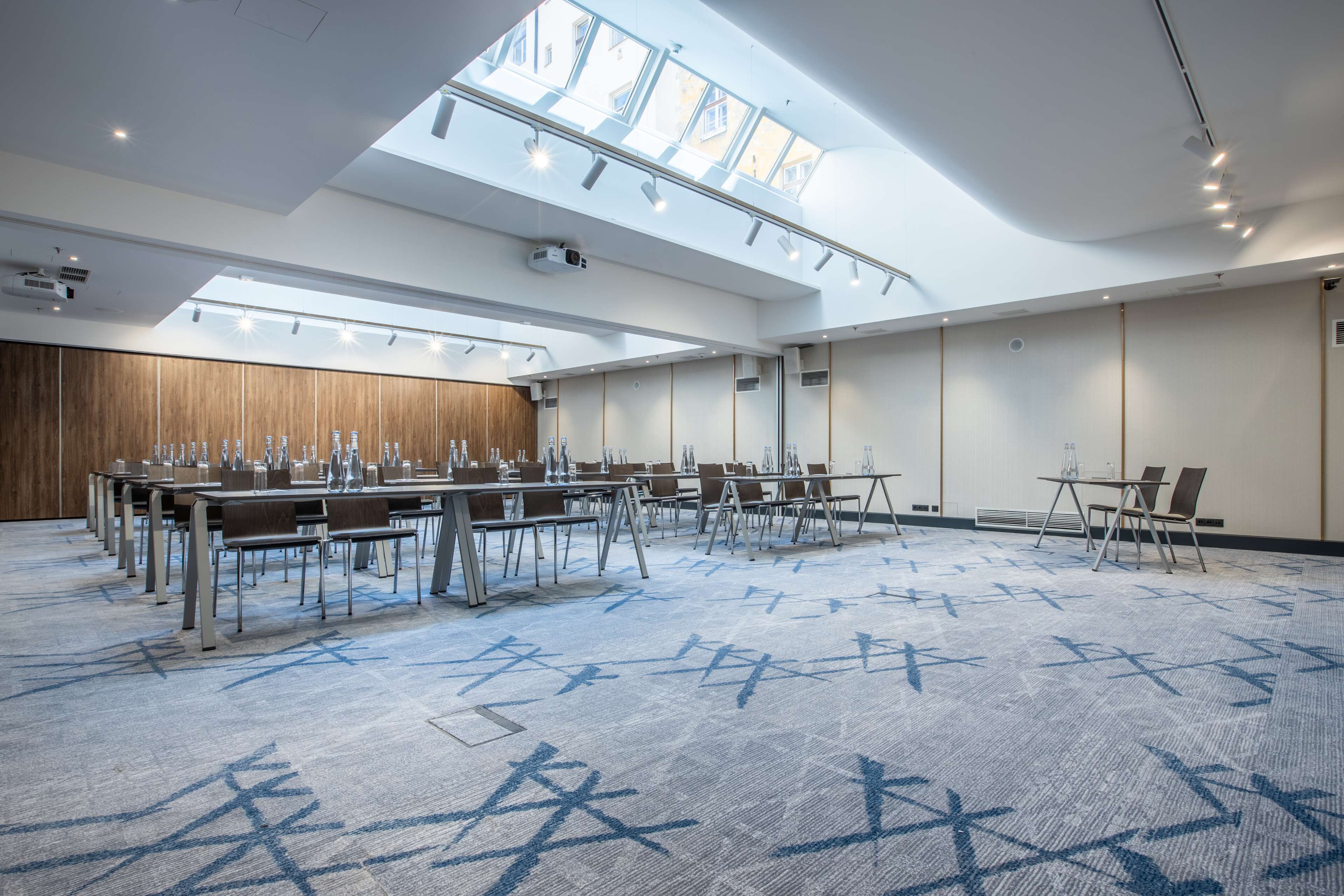 A conference room with a high ceiling, skylights, and a patterned carpet. Tables and chairs are arranged for meetings.