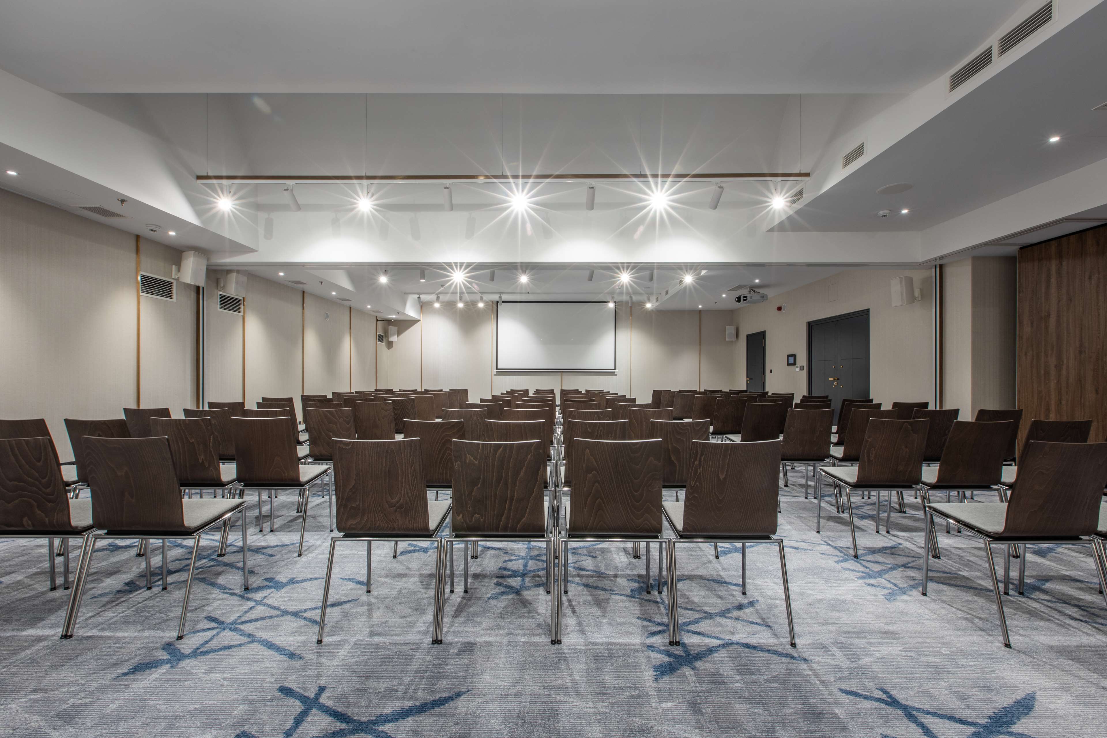 Ein Konferenzraum mit Reihen von Stühlen, einer Projektionsleinwand und einem Teppichboden.