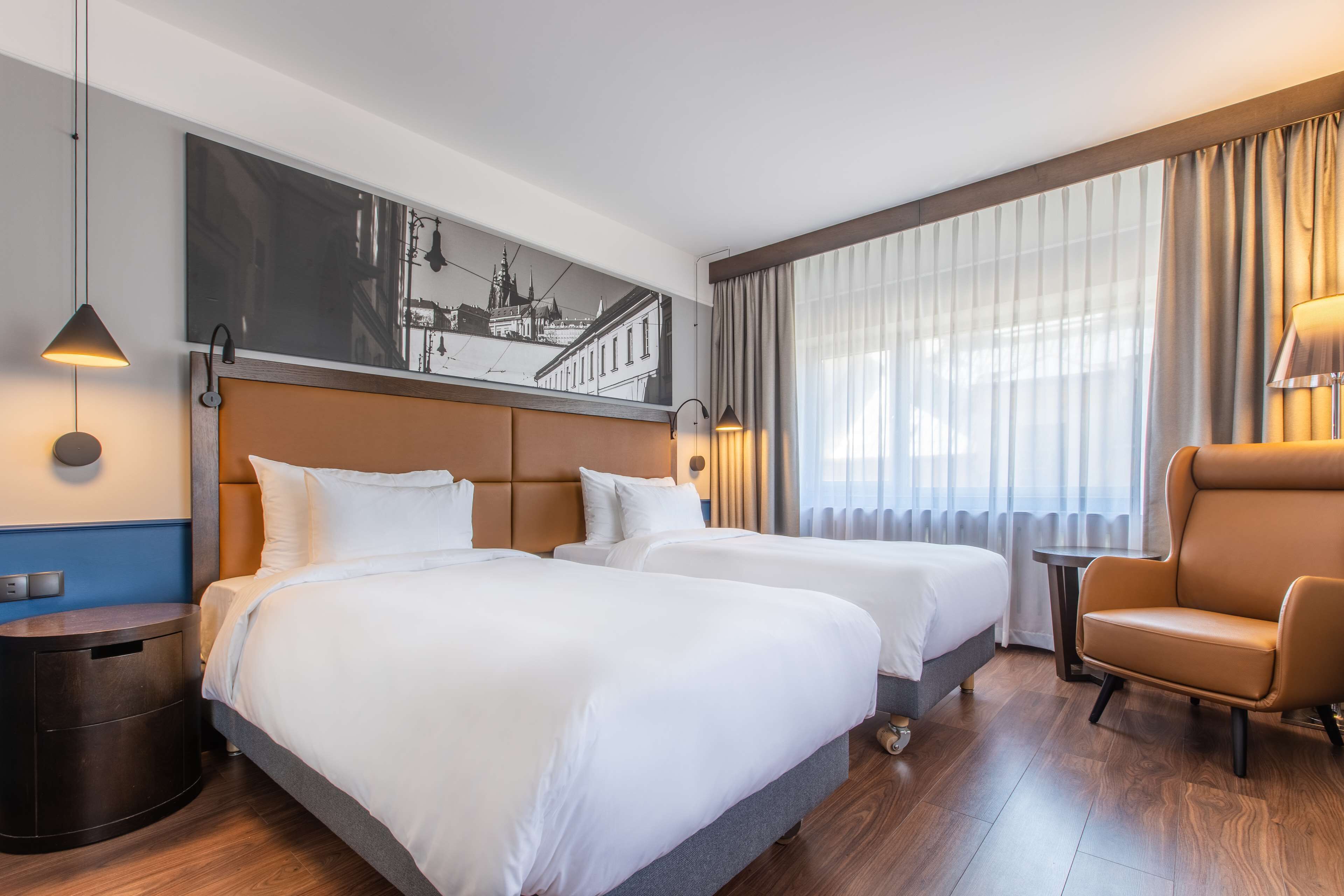 A hotel room with two beds, a large wall-mounted artwork, a wooden floor, and a chair.