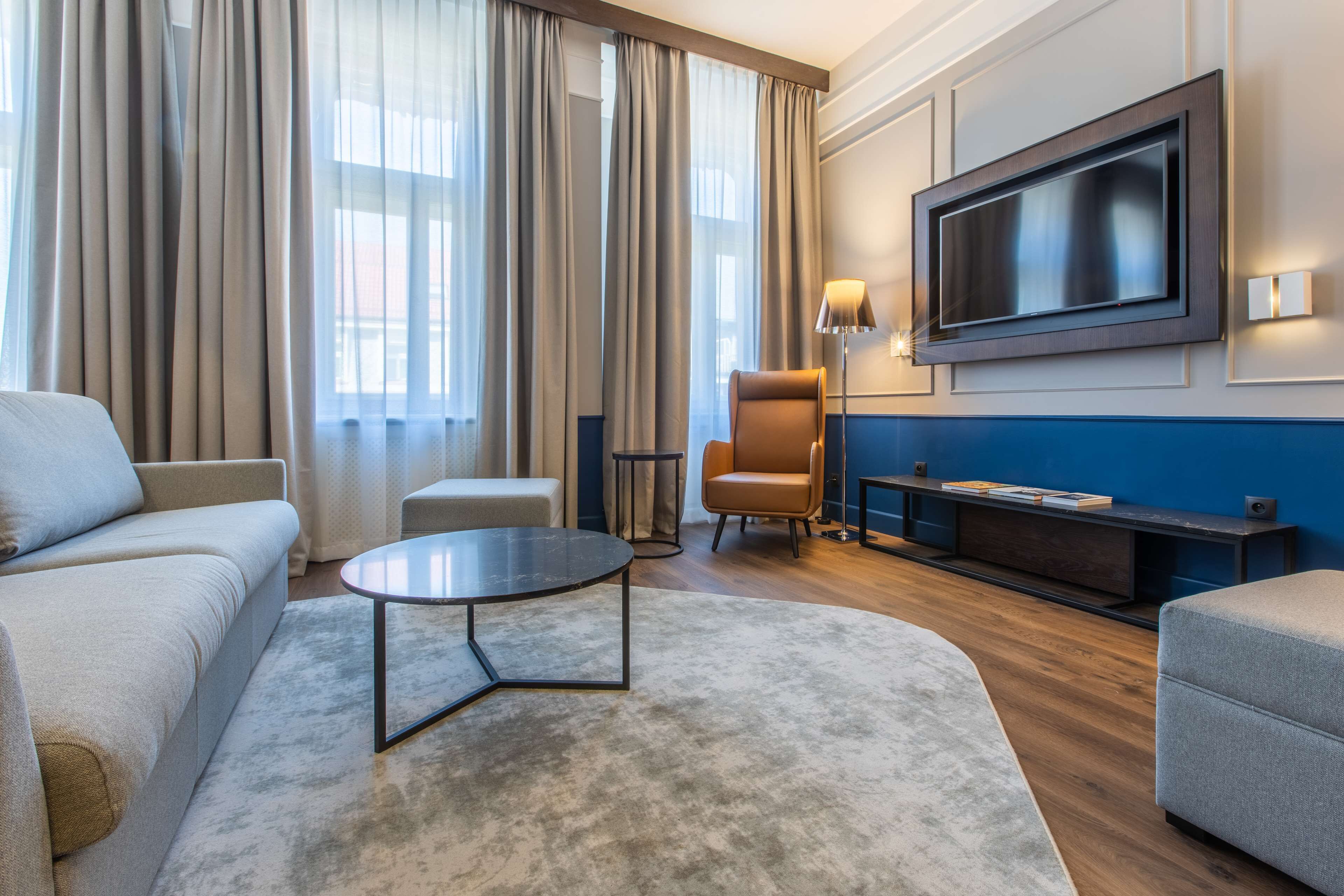 Een moderne woonkamer met een bank, fauteuil, salontafel en een flatscreen televisie aan de muur.