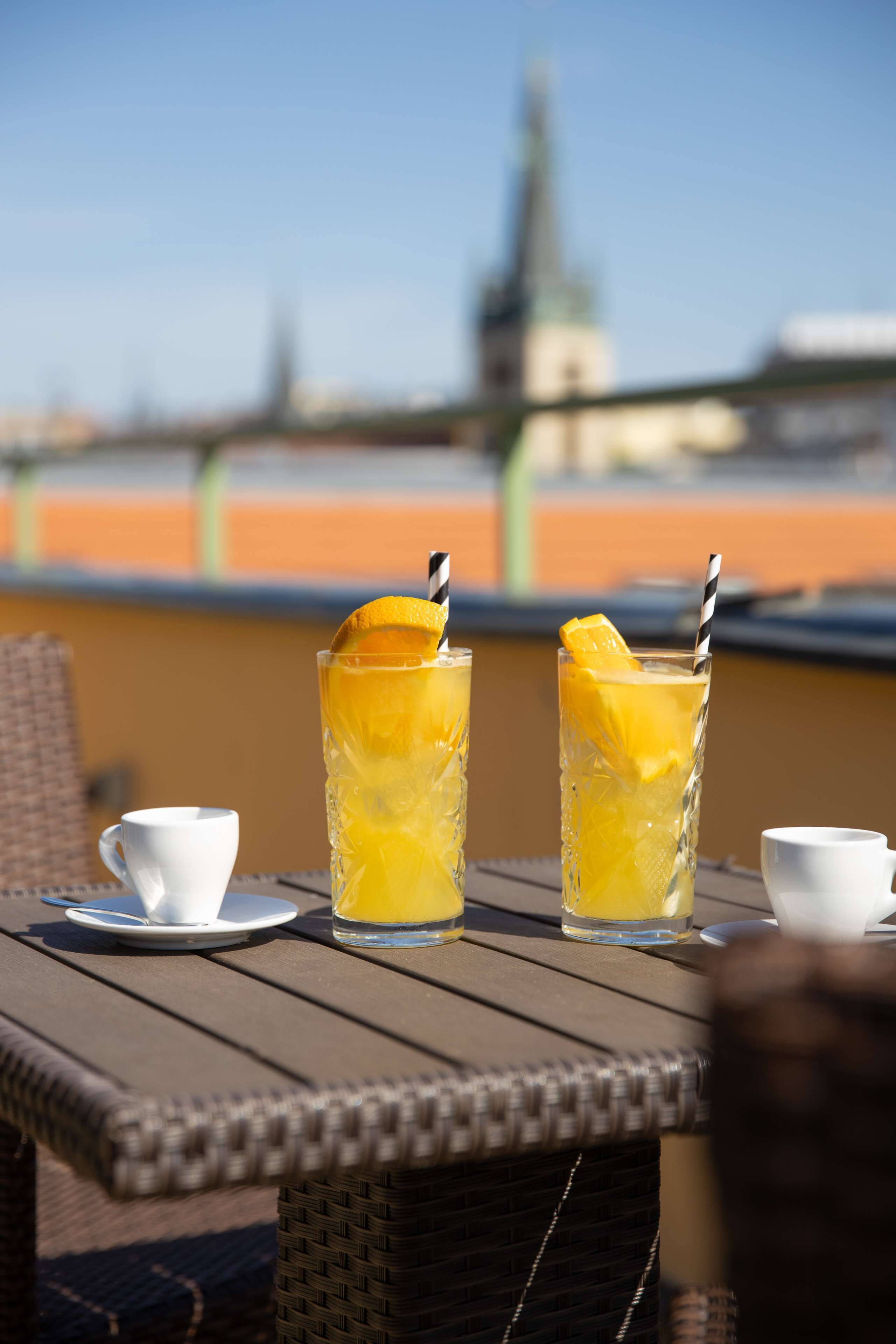 Two tall glasses of orange juice with lemon slices and straws on a wooden table.