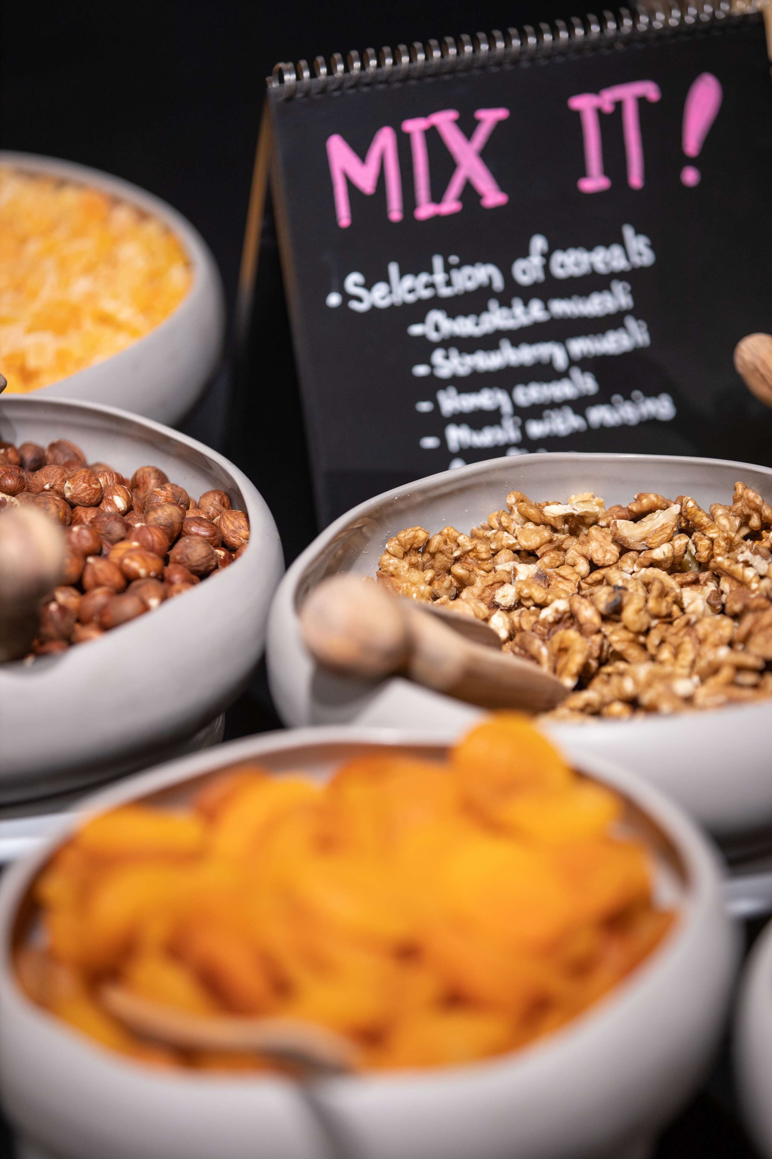 A selection of cereals in bowls with a sign that says "MIX IT!" and lists options like "Oatmeal," "Strawberry," and "Cereal with milk."