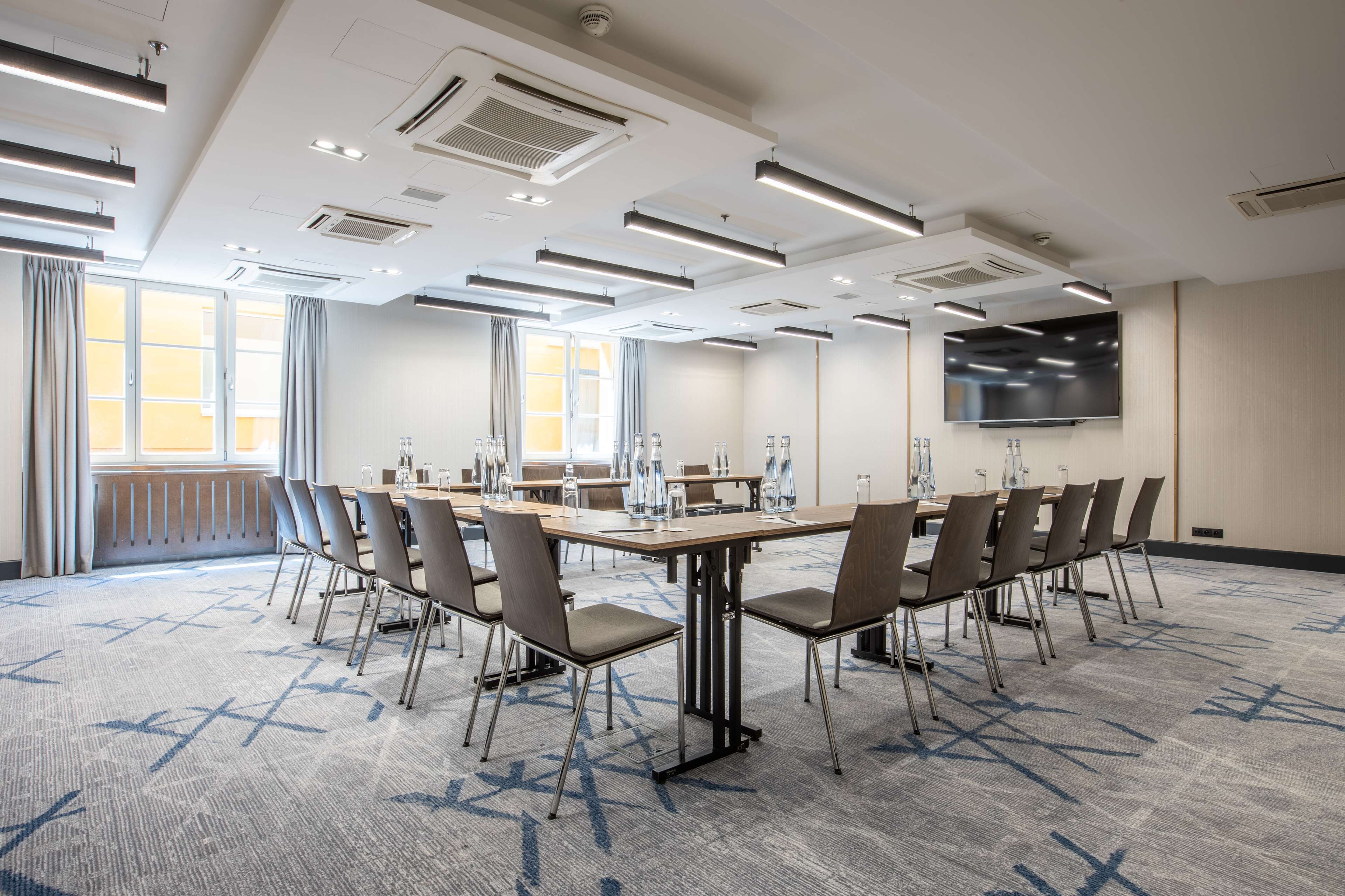 A conference room with a large table, chairs, a flat-screen TV, and a patterned carpet.