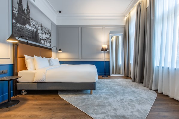 A hotel room with a large bed, a nightstand, a desk, and a painting on the wall.