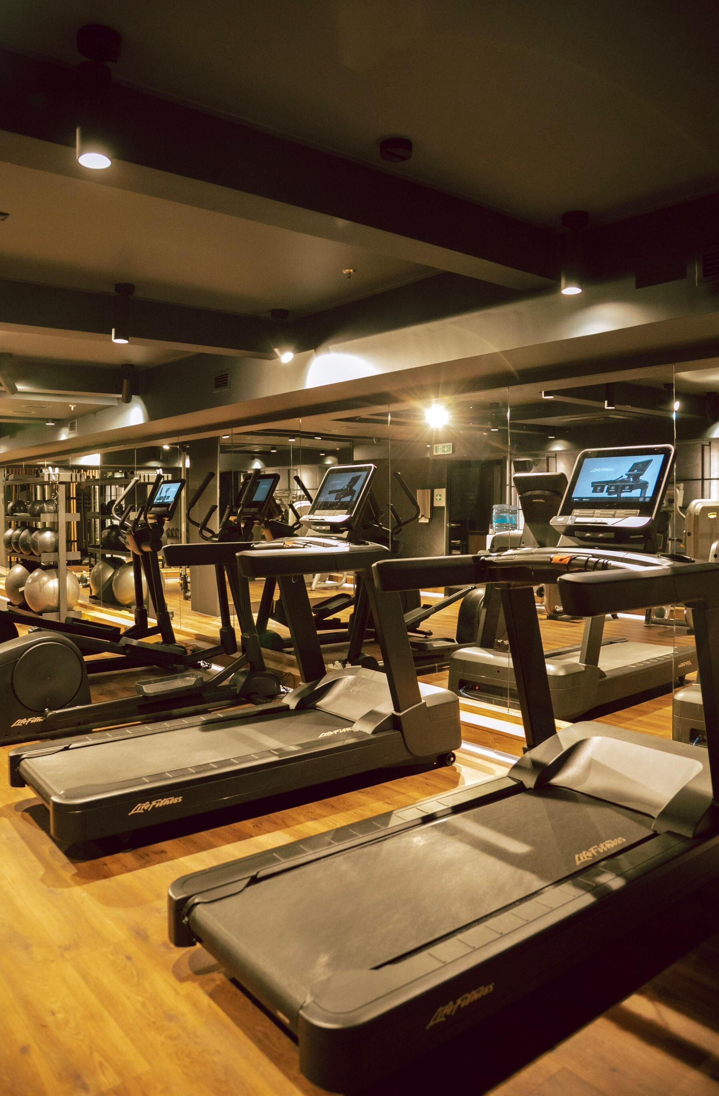 Un gimnasio con cintas de correr, bicicletas estáticas y pelotas de ejercicio.