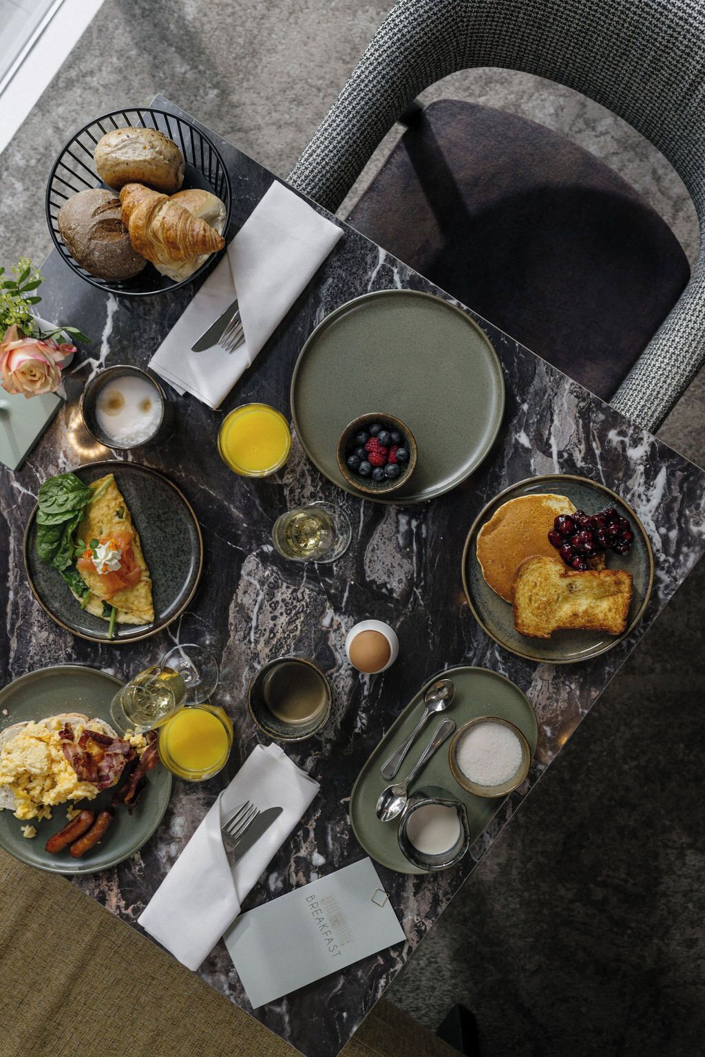 Une table en marbre dressée pour le petit-déjeuner, avec des croissants, des viennoiseries, des œufs brouillés, des toasts, des fruits rouges et du jus de fruits.