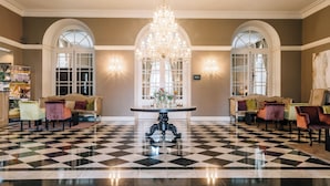 Un vestíbulo con piso a cuadros, una mesa central con candelabro, y asientos a ambos lados.