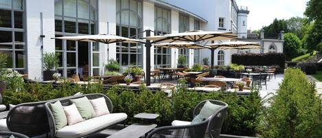 An outdoor patio with wicker furniture, potted plants, and umbrellas.