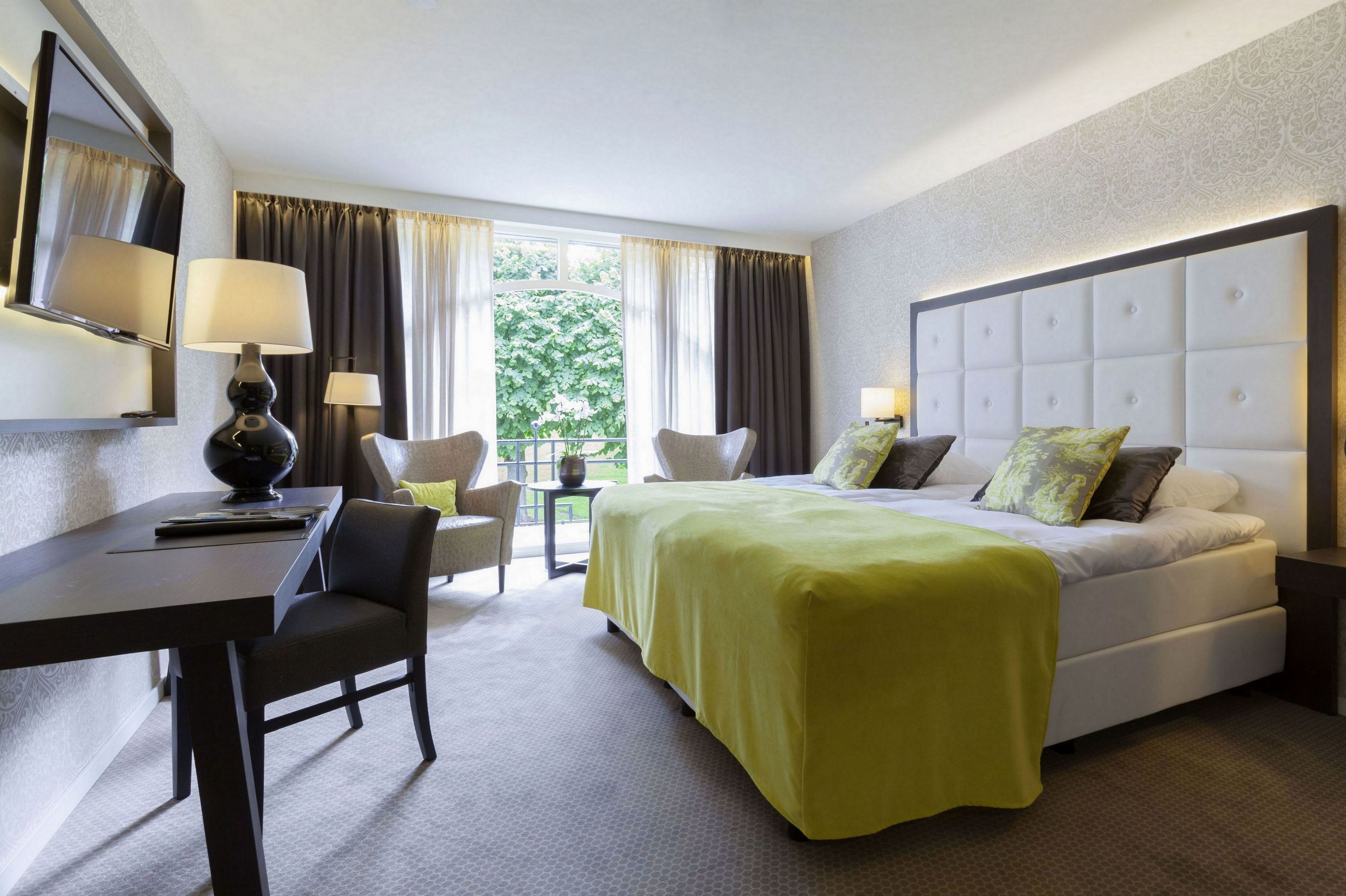 A hotel room with a bed, a desk, a chair, and a window with curtains.
