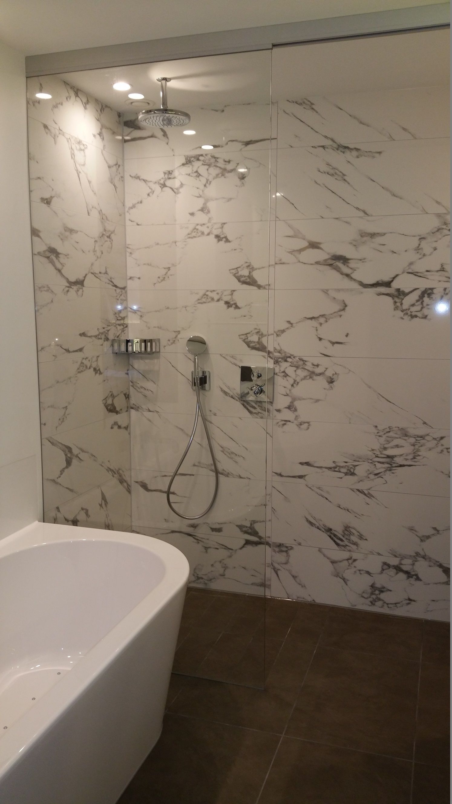 Une salle de bain moderne avec une baignoire sur pieds, un espace de douche clos par des parois de verre et doté d’un pommeau de douche à main, et des murs à motifs de marbre.