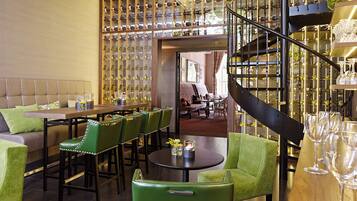 Ein Restaurantinneres mit einem langen Esstisch, grünen Sitzmöglichkeiten, einer Wendeltreppe und Weinkühlschränken.