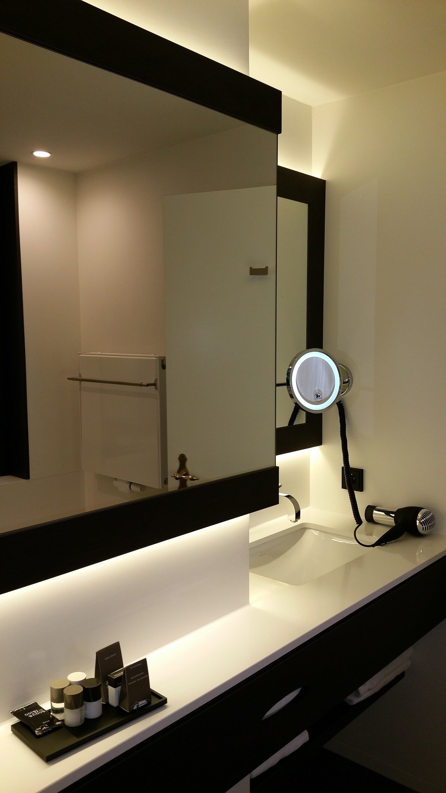 A modern bathroom with a large mirror, a sink, and a hairdryer on the counter.