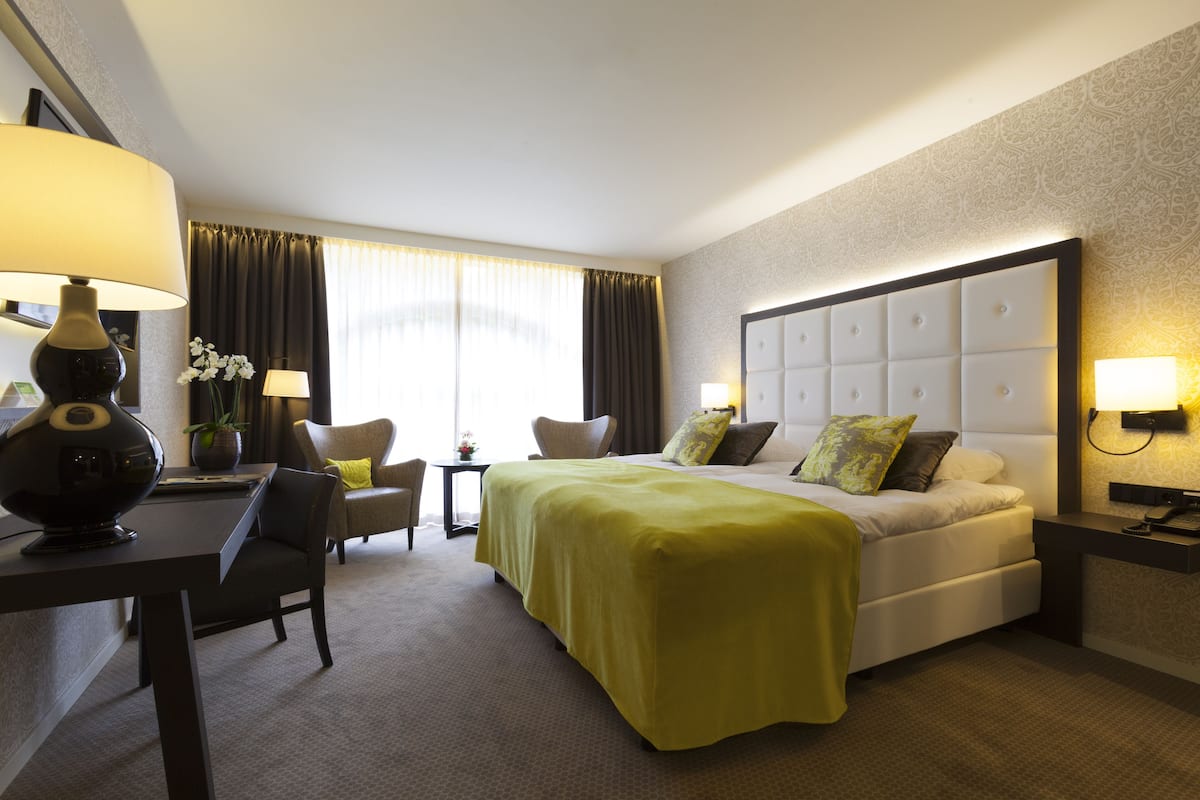Una habitación de hotel con cama, escritorio, silla, lámpara y mesita de noche.