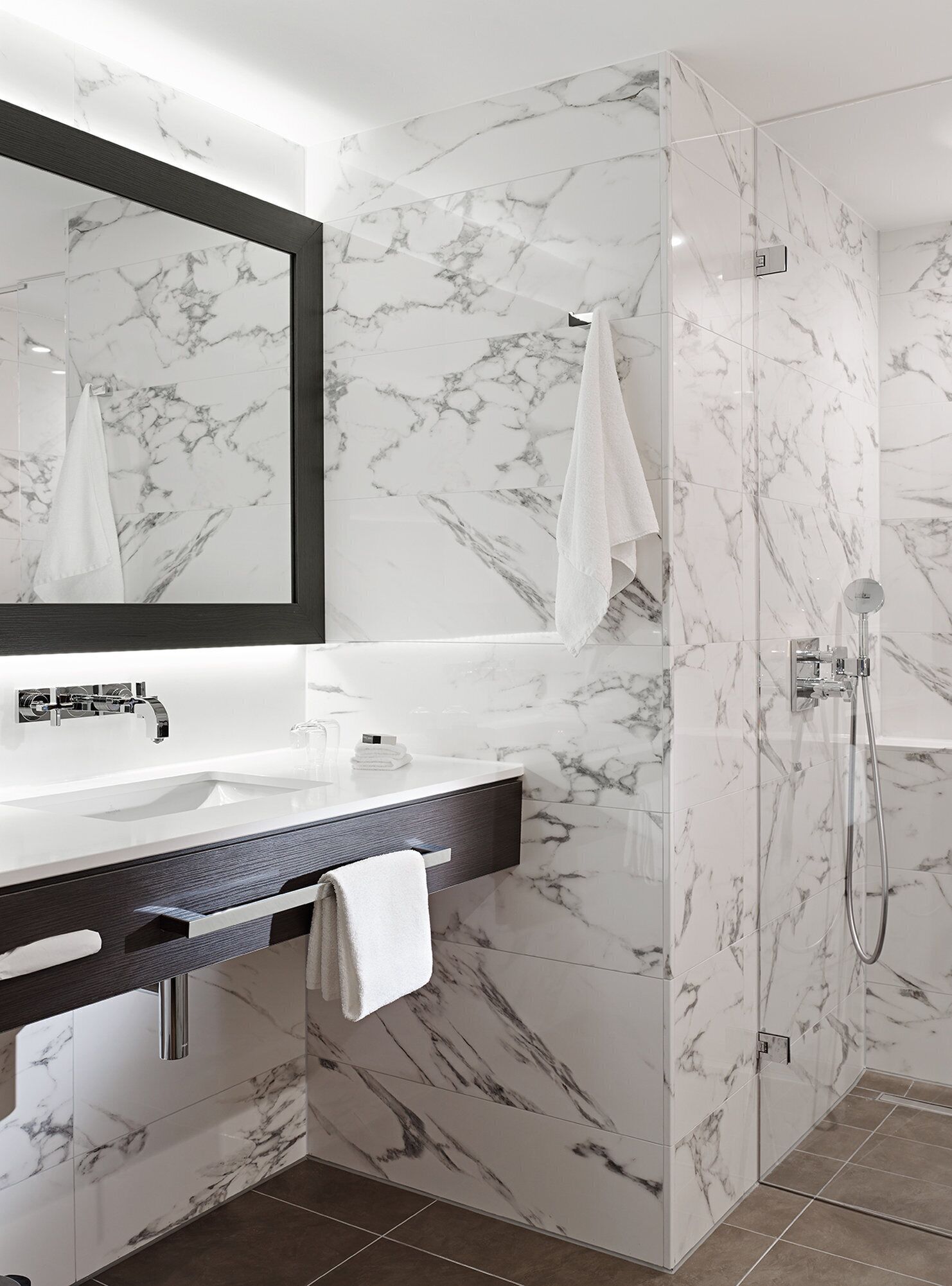 A modern bathroom with a marble vanity, a large mirror, a shower, and a towel rack.