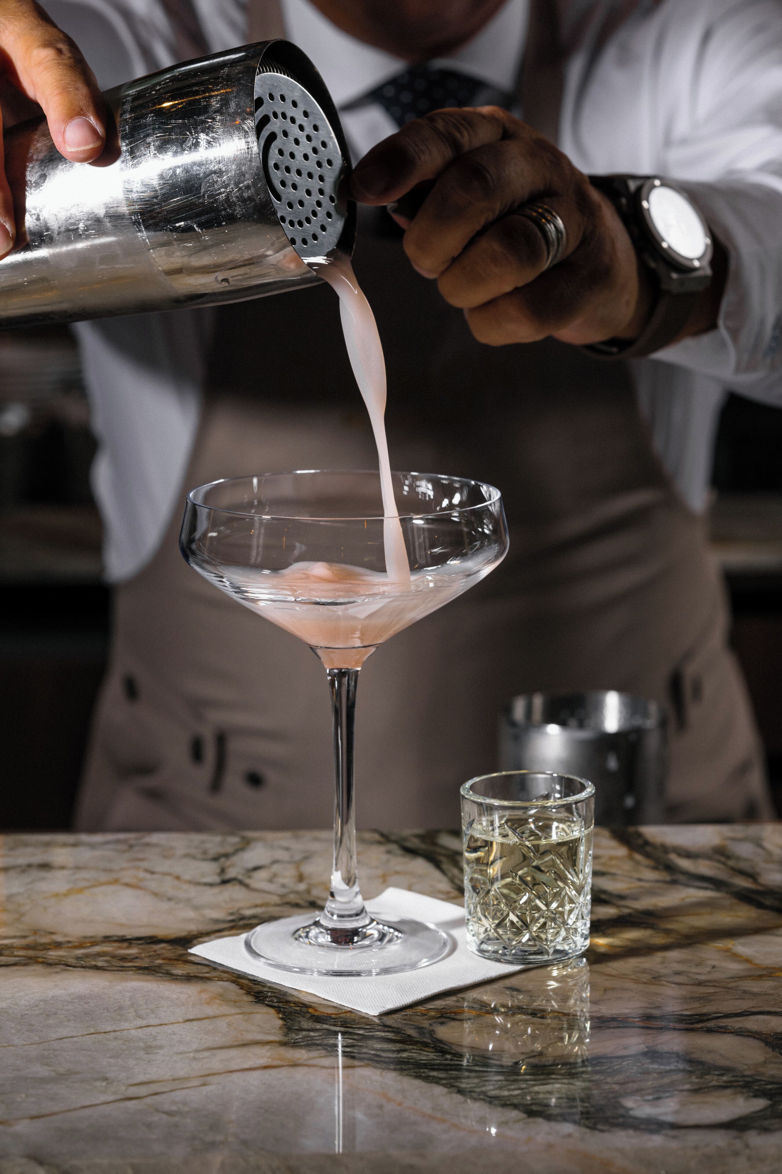 Un barman vertiendo una bebida en una copa de martini.