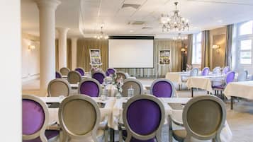 A conference room with tables and chairs, a projector screen, and a chandelier.
