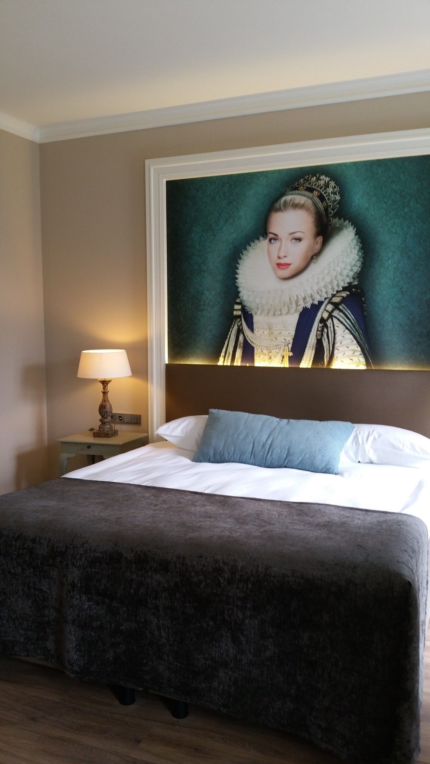 Une chambre d’hôtel avec un grand lit, une table de chevet avec une lampe et un portrait encadré accroché au mur.