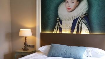 Une chambre d’hôtel avec un grand lit, une table de chevet avec une lampe et un portrait encadré accroché au mur.