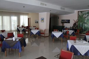 Comedor con mesas dispuestas para el servicio, sillas y un amplio ventanal con cortinas.