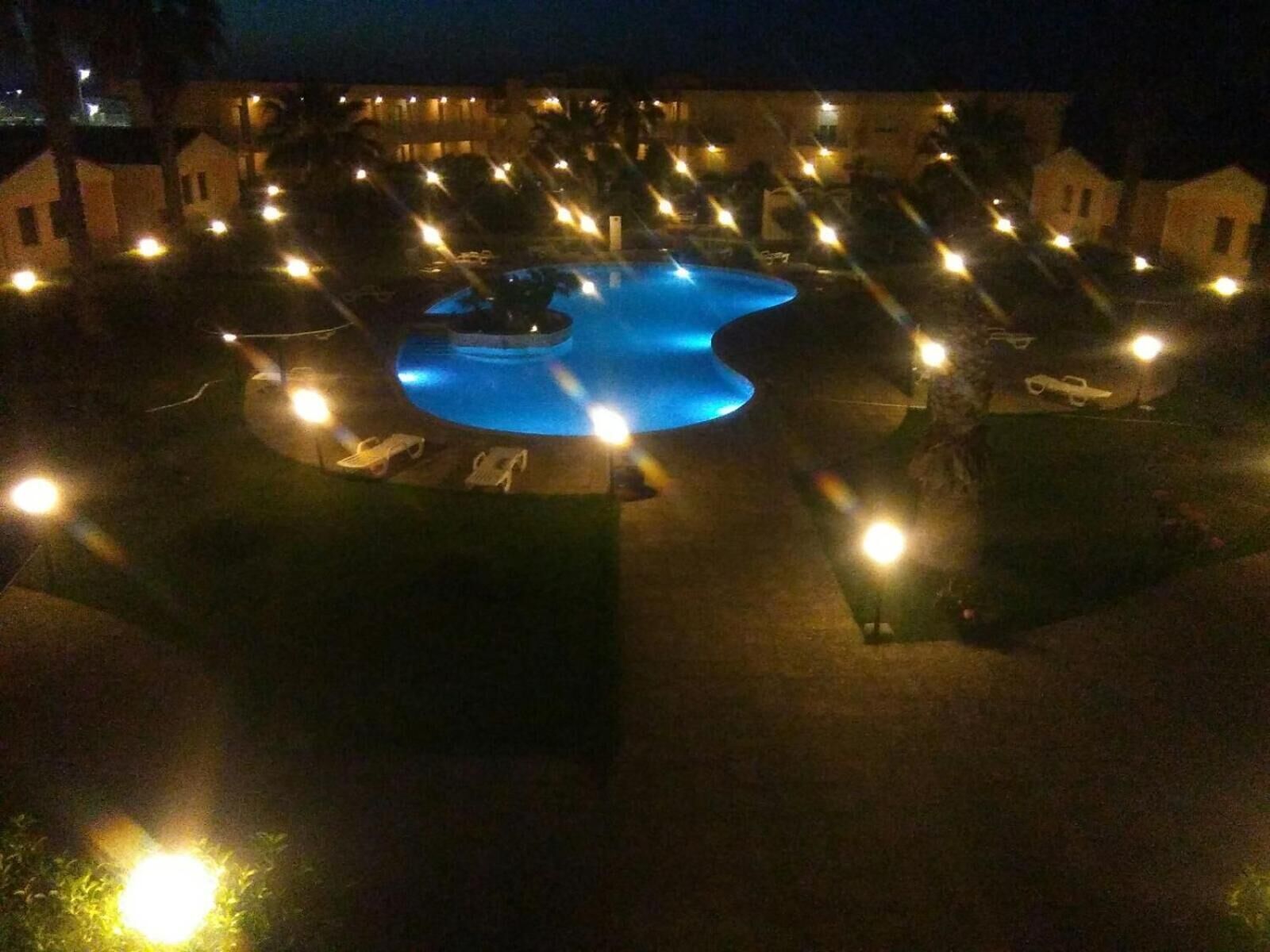 Un espace piscine de forme circulaire, entouré de chaises longues et de petits bâtiments, qui fait probablement partie d’un hôtel ou d’un complexe touristique.
