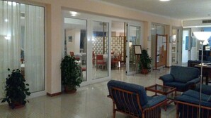 A spacious lobby with a seating area, a dining area visible through glass doors, and potted plants. - Hotel Minerva (Brindisi)