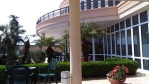 An outdoor patio area with a curved balcony, outdoor seating, and a trash bin. - Hotel Minerva (Brindisi)
