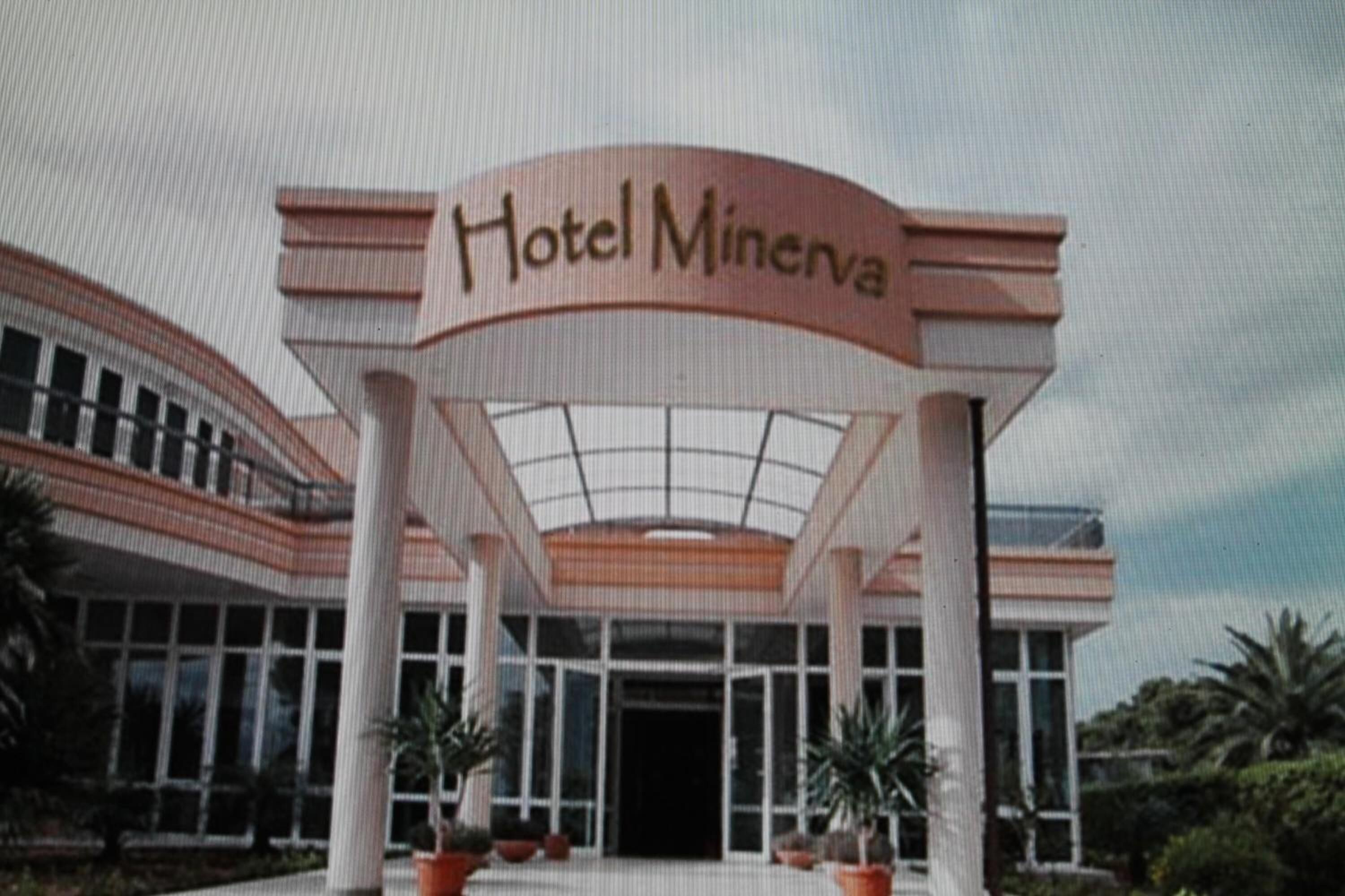 Entrada de un hotel con un gran letrero que dice "Hotel Minerva", con un diseño moderno que incluye una cubierta de vidrio y columnas.