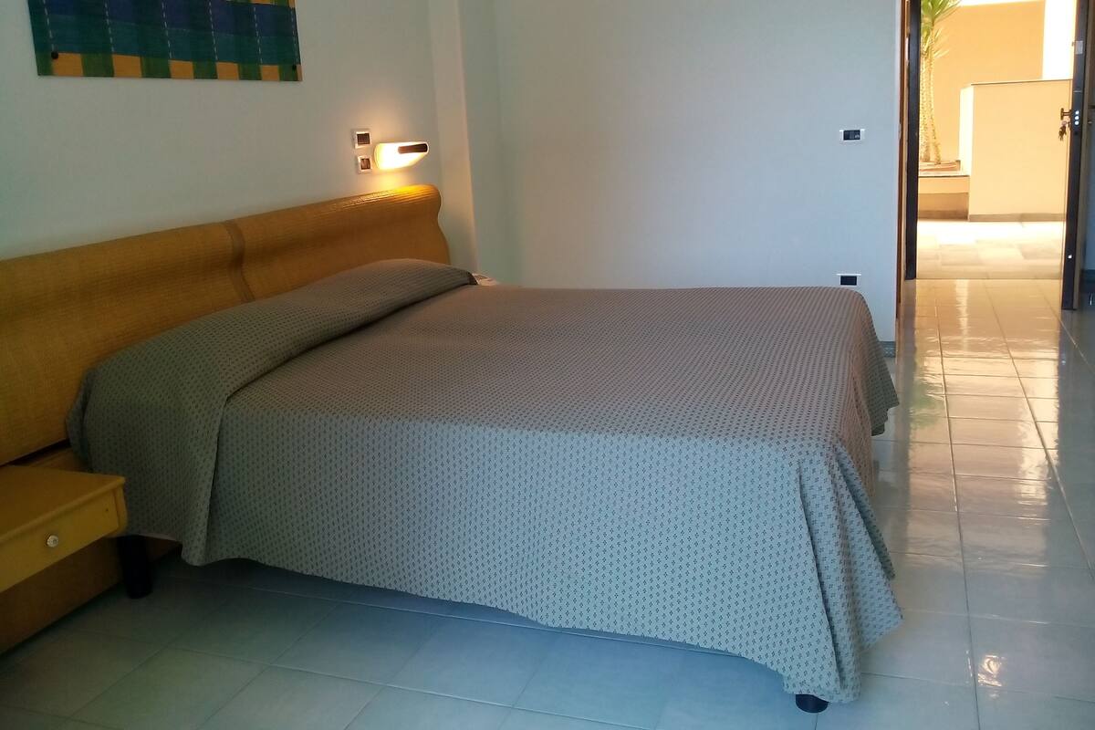 A bedroom with a bed, a nightstand, and a wall-mounted light fixture.