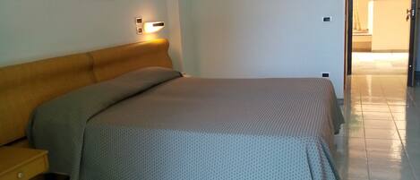 A bedroom with a bed, a nightstand, and a wall-mounted light fixture.