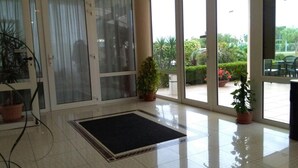 A hotel lobby with a large glass door, a black mat at the entrance, and potted plants. - Hotel Minerva (Brindisi)