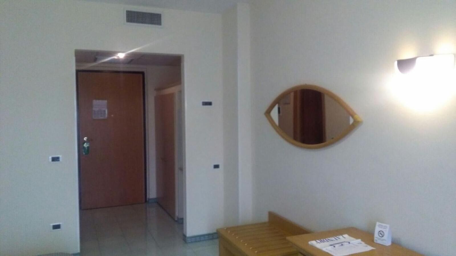 A hotel room with a wooden door, a mirror on the wall, and a small table with a chair.