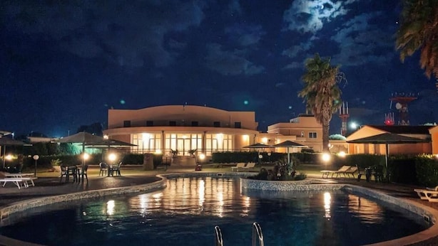 A nighttime pool area with a circular pool, lounge chairs, and umbrellas. - Hotel Minerva (Brindisi)