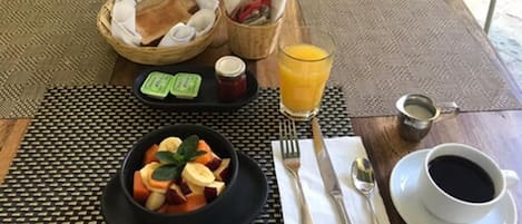 A breakfast setting with a bowl of fruit, toast, jam, and juice on a table with a placemat.