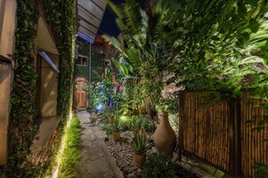 Un sendero estrecho bordeado de abundante vegetación y plantas en macetas, que conduce a una puerta de madera.