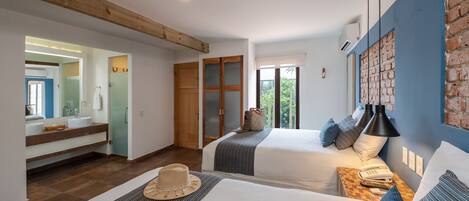 Habitación de hotel con dos camas, un baño con un espejo grande y vistas a zonas verdes.