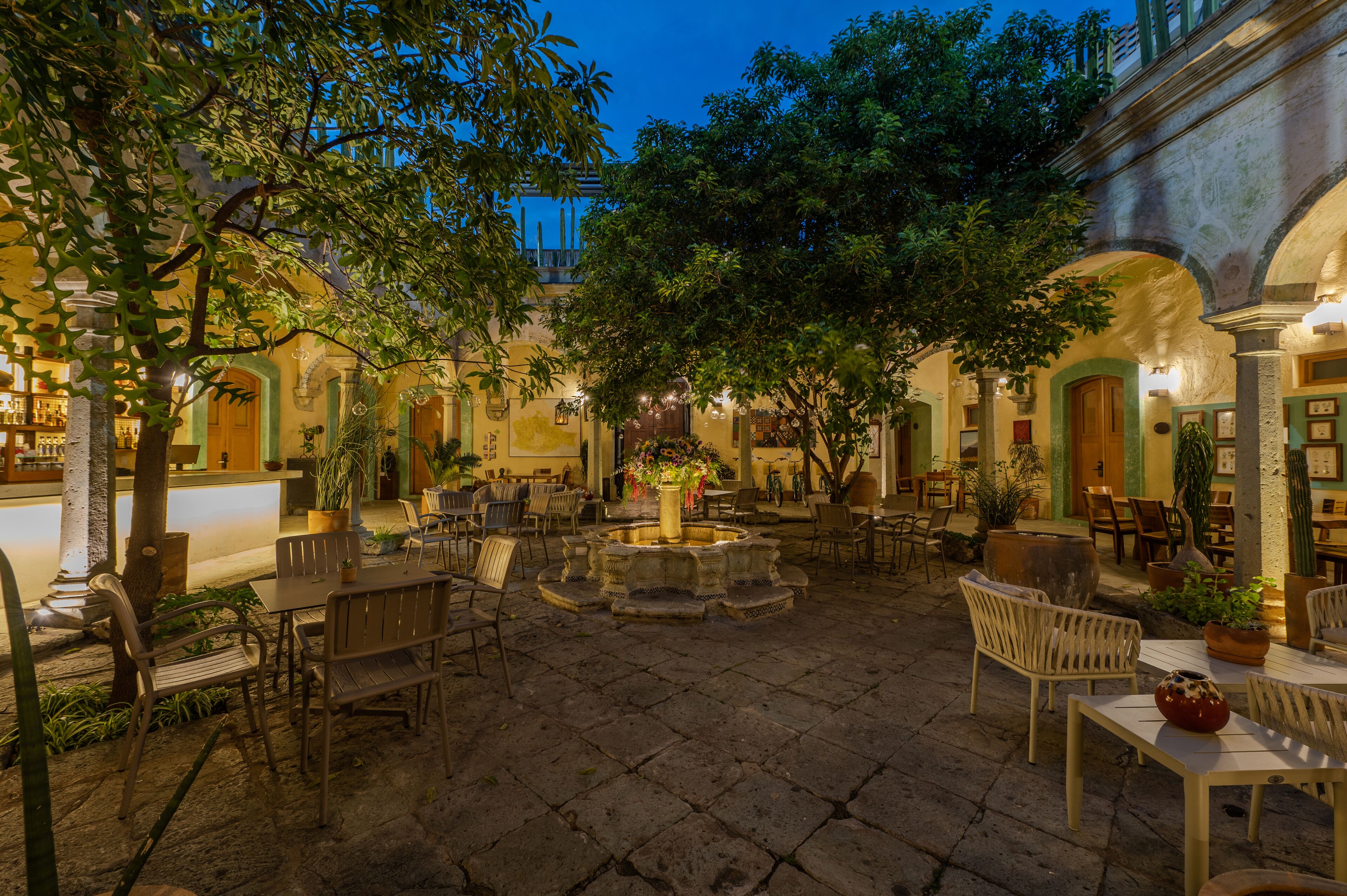 An outdoor courtyard with stone flooring, seating arrangements, and a central water feature.