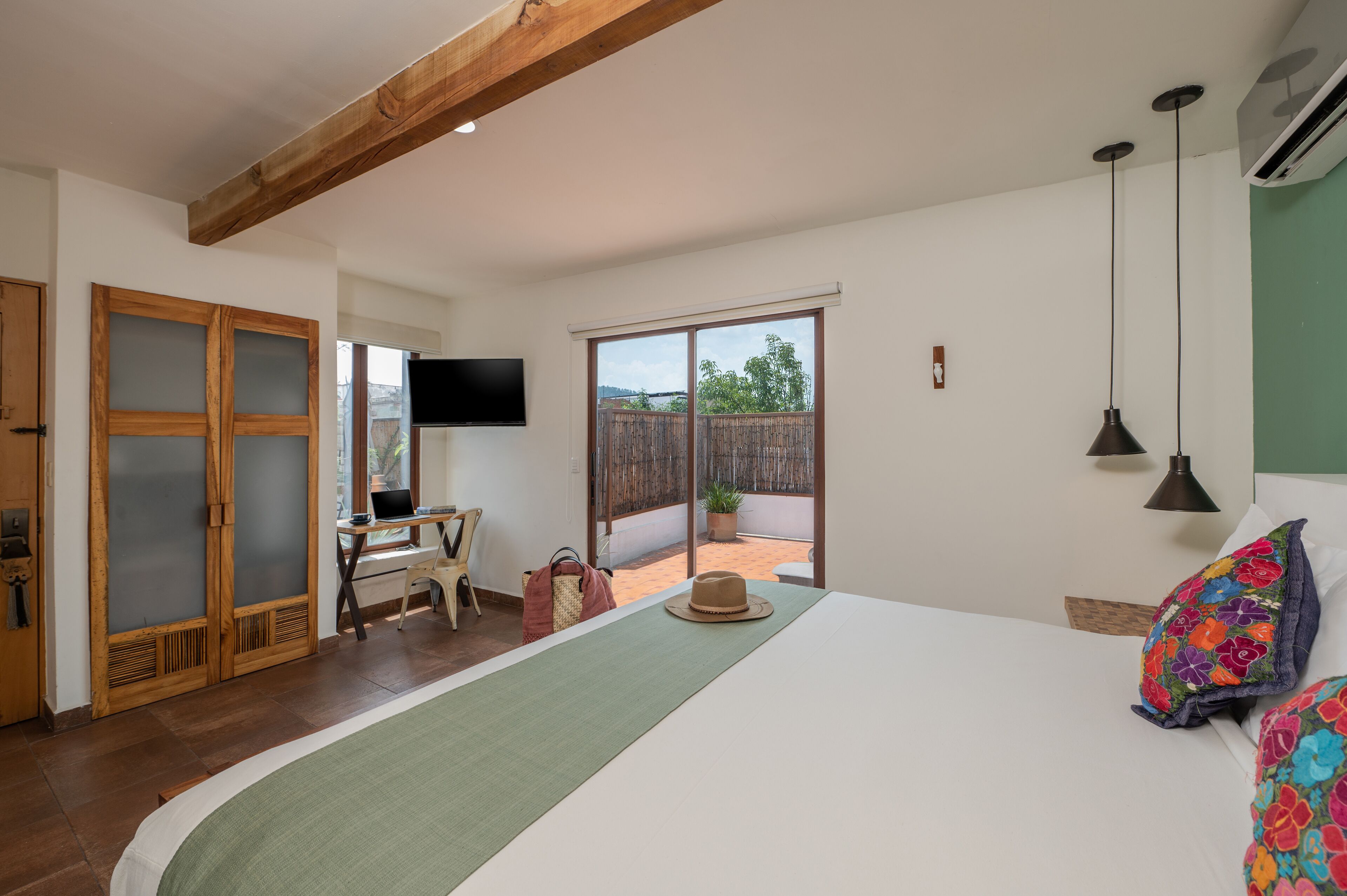 Een slaapkamer met een groot bed, een bureau met een laptop, een televisie en een schuifpui naar een balkon.