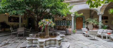 Un patio con una fuente, zona de estar y plantas en macetas.