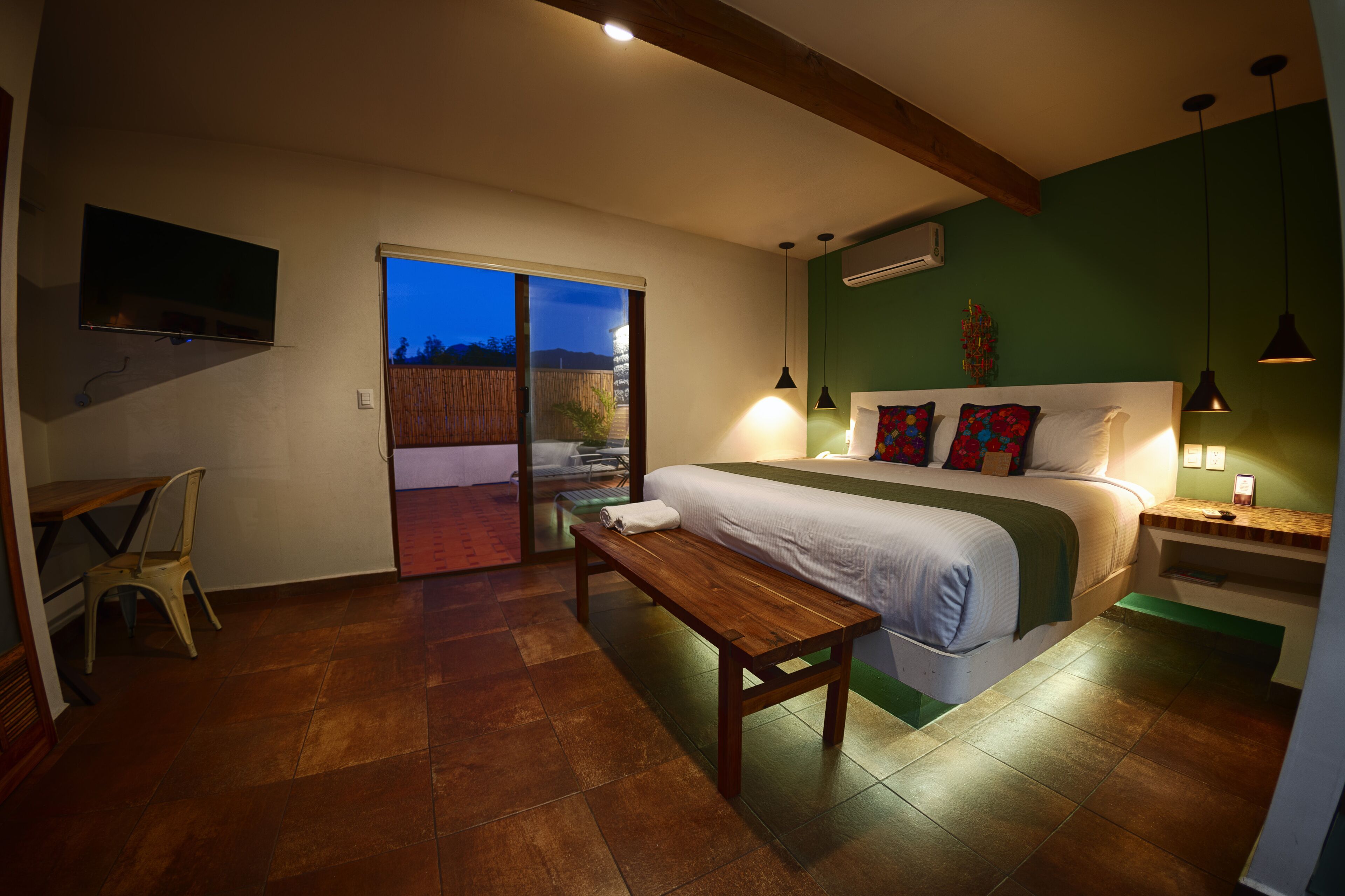 A bedroom with a large bed, a bench, a desk, and a TV.